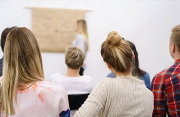 Weiterbildungen für Fachkräfte. Bild zeigt teilnehmende Gruppe von Personen von hinten. Im Hintergrund ist eine Frau zu sehen, die an einer Tafel steht und referiert.