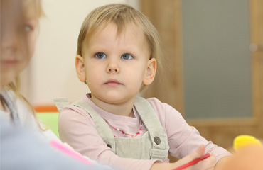 BSL ist eine offene Anlaufstelle für Eltern. Bild zeigt zwei erwachsene Frauen im Gespräch. Im Vordergrund spielt ein Kind auf dem Teppich mit Kuscheltieren.