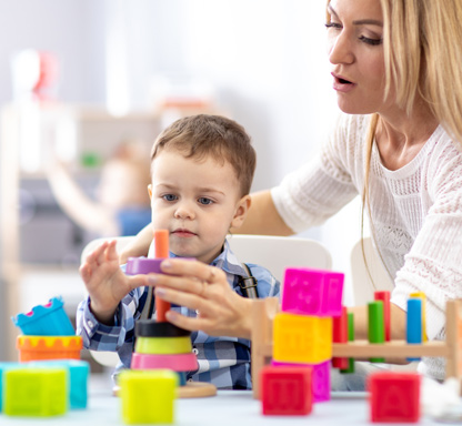 Sozialpädagogische Familienhilfe. Bild zeigt Kind, dass mit farbigen Bauklötzen spielt. Es wird von einer Frau beim Stapeln unterstützt.