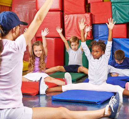 Vereinsangebote für Familien. Bild zeigt Kinder in einem Gymnastikraum mit Trainerin, die Übungen vormacht.