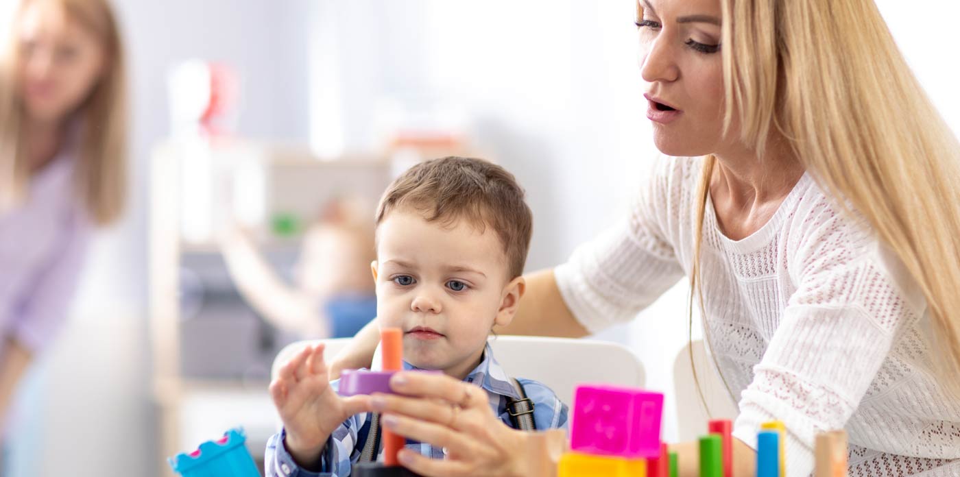 Sozialpädagogische Familienhilfe. Bild zeigt Kind, dass mit farbigen Bauklötzen spielt. Es wird von einer Frau beim Stapeln unterstützt.