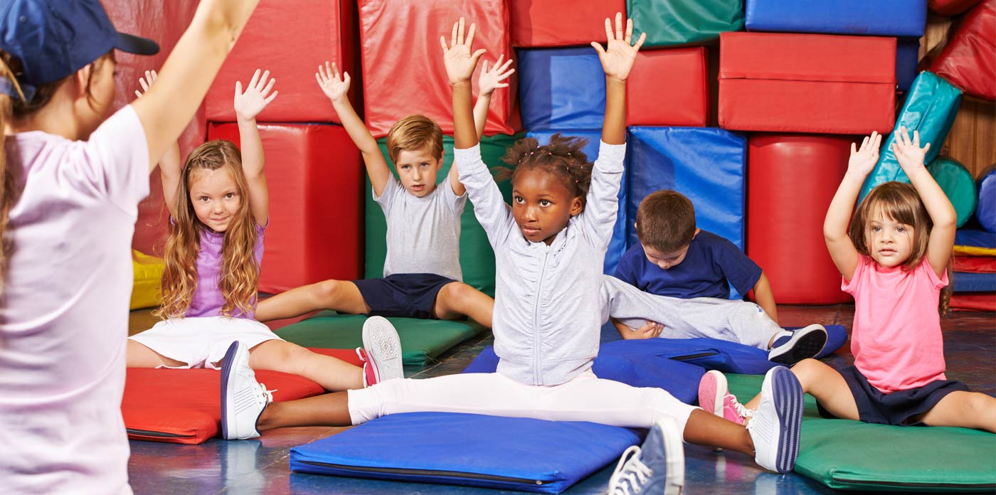 Vereinsangebote für Familien. Bild zeigt Kinder in einem Gymnastikraum mit Trainerin, die Übungen vormacht.